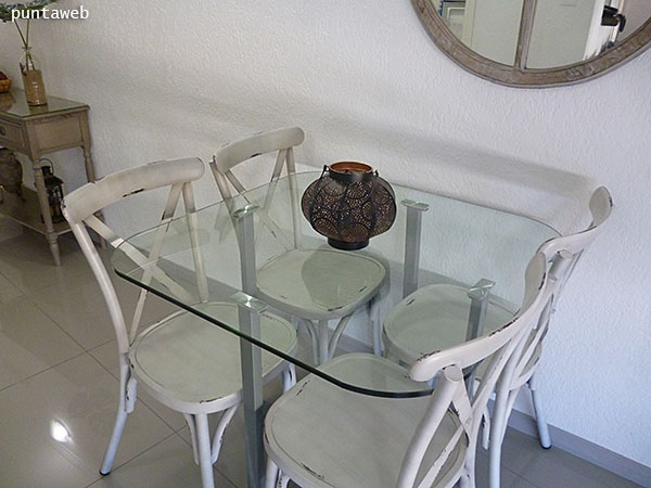 Square table detail with rounded corners in glass with four individual armchairs.