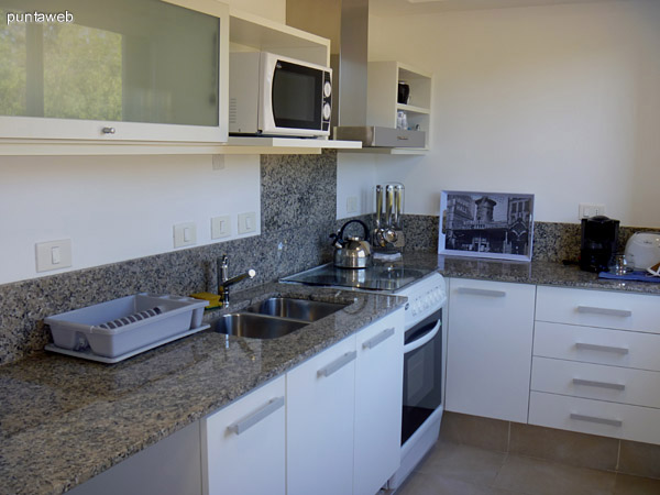 Cocina con mesada en L de granito, muebles sobre y bajo mesada de nivel, equipada con electrodomésticos de igual perfil.