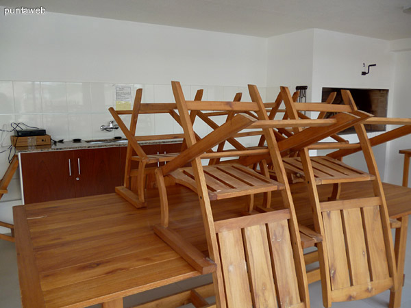 Salón común con 2 parrilleros, mesas, sillas y heladera. 
