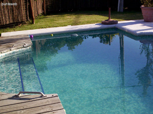 Detalle del cerco móvil en la piscina al aire libre climatizada.<br><br>Al fondo de la imagen, conjunto de muebles de jardín en madera.